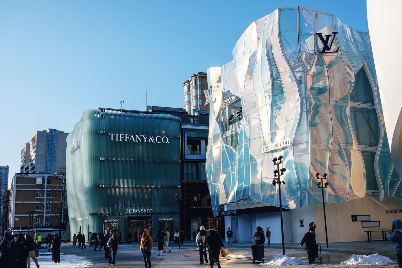 services-03 Outdoor view of Tiffany & Co and Louis Vuitton stores in a bustling city plaza.