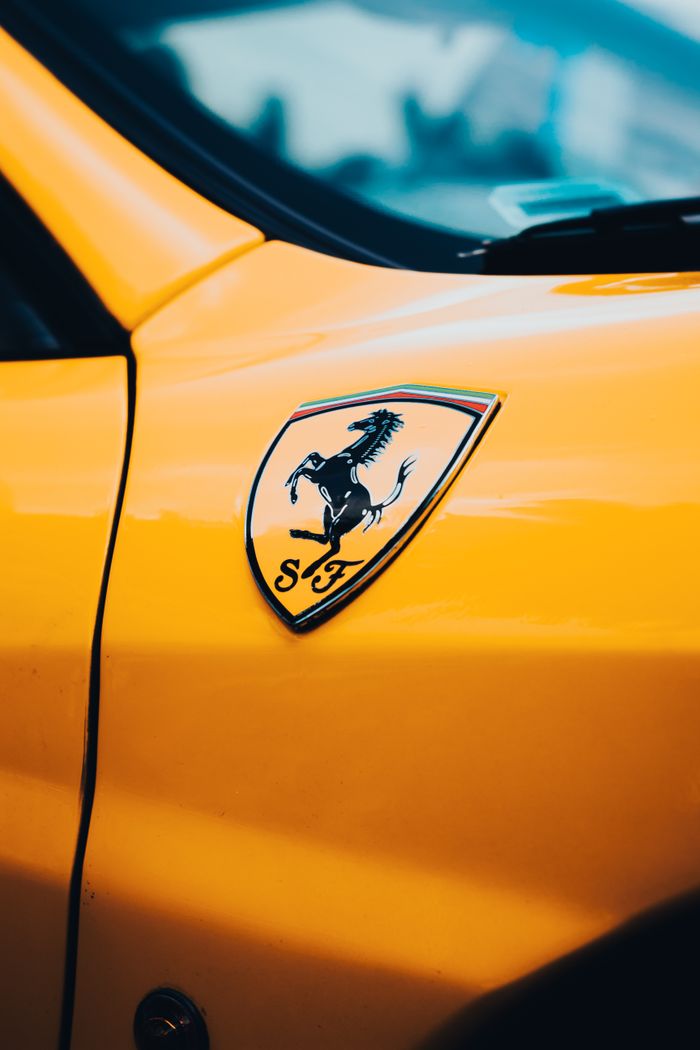 about-us-01 Detailed close-up of a Ferrari logo on a vibrant yellow cars body.